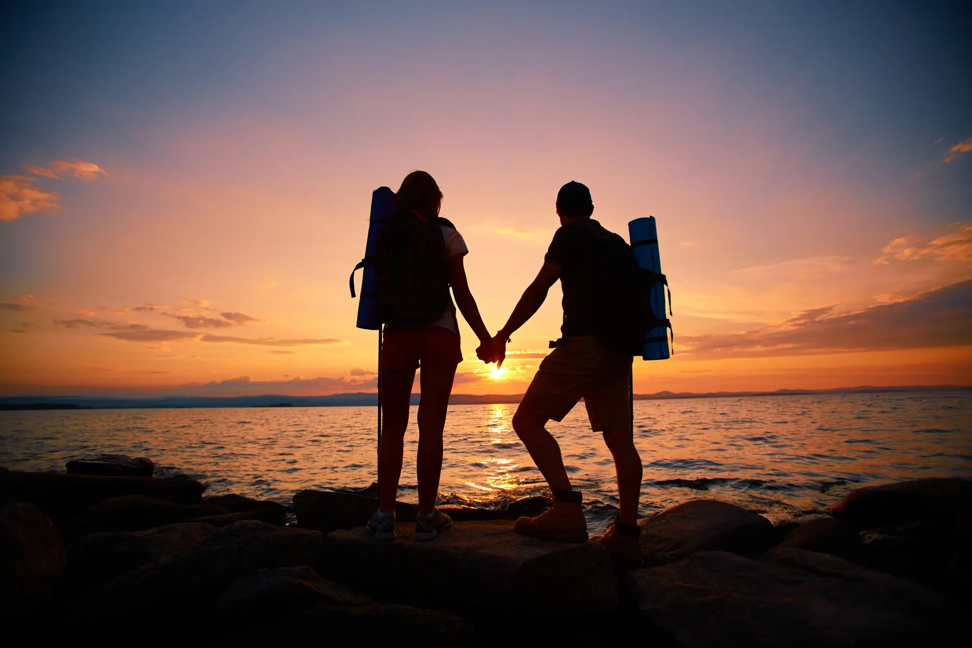 Couple holding hands at sunset with backpacks